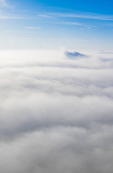 Воздушное фото над туманом или белыми облаками с сияющим солнцем. С воздуха небо облачно с восходом солнца. Над облаками из окна самолета или беспилотника. - Фото, изображение