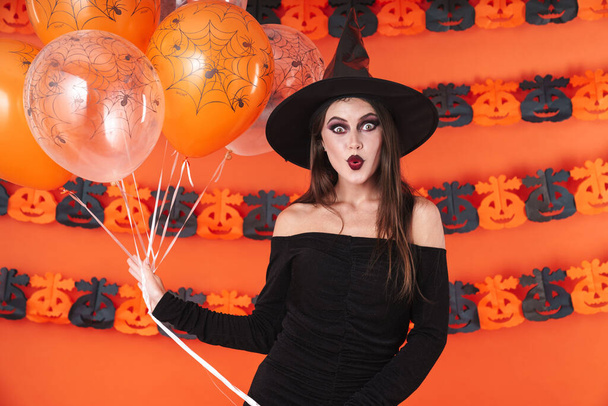 Image of witch girl in black halloween costume holding balloons - Photo, image
