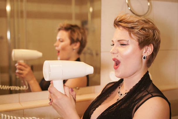 Fotografie radostné ženy, jak si suší vlasy po umytí v koupelně u zrcadla. - Fotografie, Obrázek