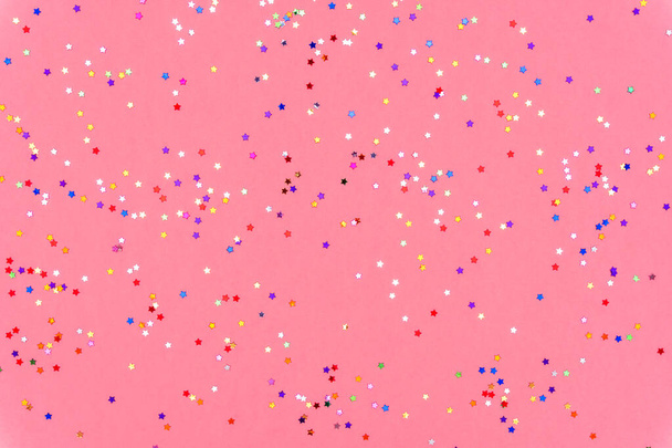 Φωτογραφία από πολύχρωμα αστέρια glitter ψεκάζει σε ροζ μοντέρνο φόντο. Εορταστικό φόντο διακοπών για τα έργα σας. Έννοια εορτασμού. Χριστουγεννιάτικο μοτίβο. Πάνω άποψη, επίπεδη lay - Φωτογραφία, εικόνα