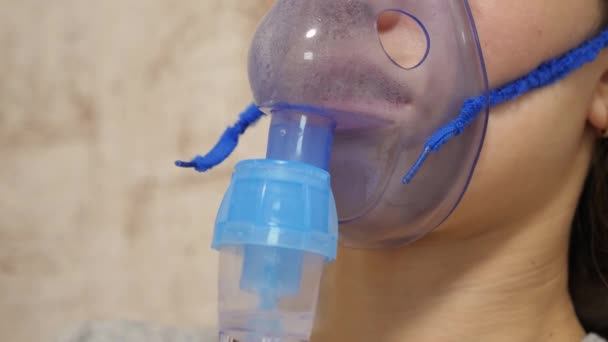 Bir hastanede yüzüne solunum maskesi takılmış bir kadın tedavi ediliyor. Hasta kız kanepede oturan bir nebulizör tarafından solunuyor. Maskeli kadın. Solunum yolu için ciğerlere buhar çek. Öksürük tedavisi - Video, Çekim