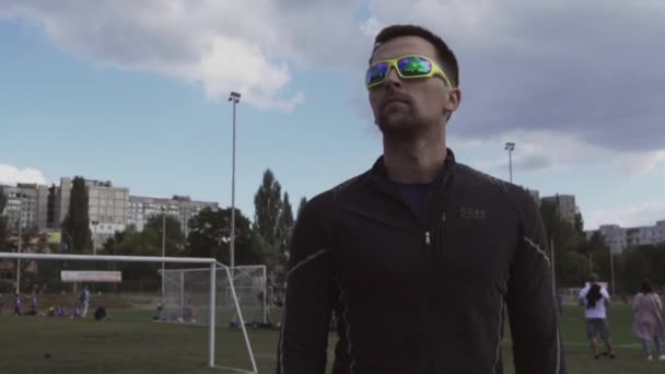 March 2, 2019. Theme sport and health. Portrait of a young caucasian man in sportswear and sunglasses. Training sports lesson at city stadium track treadmill. Runner jogging outdoors - Video