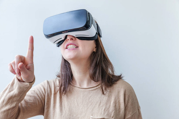 Sonríe mujer joven usando realidad virtual gafas VR casco auriculares sobre fondo blanco. Smartphone con gafas de realidad virtual. Tecnología, simulación, alta tecnología, concepto de videojuego. - Foto, imagen