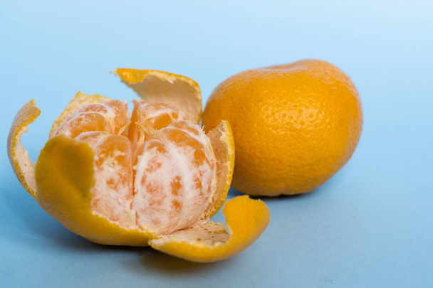 オレンジマンダリン,クレメンティーヌ, 1つの皮をむいたタンジェリンと青の背景に隔離された葉で半分にカット - 写真・画像