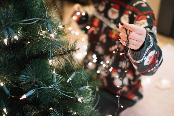 Girls hand putting Christmas lights to tree - Foto, imagen
