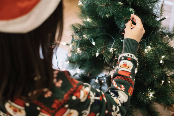 Girls hand putting Christmas lights on green tree - Photo, image