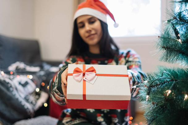 Woman holding gift box near Christmas tree - Foto, afbeelding