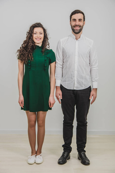 Full-length portrait of beautiful young couple standing side by side together and smiling at camera isolated on white background. - Fotó, kép