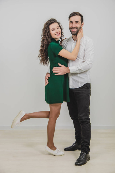 Young couple embracing and posing on white background, woman slightly raising her leg. - Foto, immagini