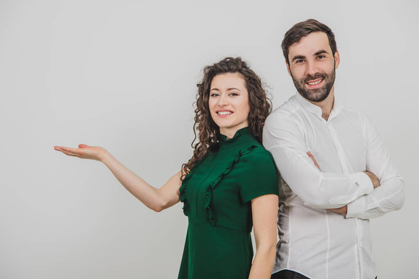 Group of two people on white background standing back to back, man folded hands, woman pointing her hand to the side, palm opened with copyspace for a product. - Фото, зображення