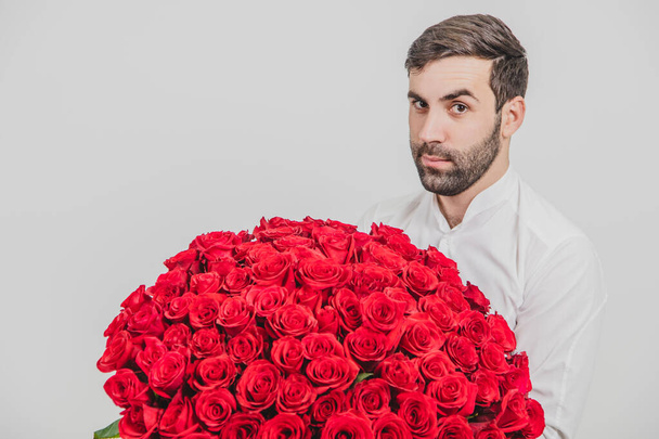 Ritratto ravvicinato di elegante uomo barbuto con in mano un mazzo di rose rosse per San Valentino, isolato su sfondo bianco
. - Foto, immagini