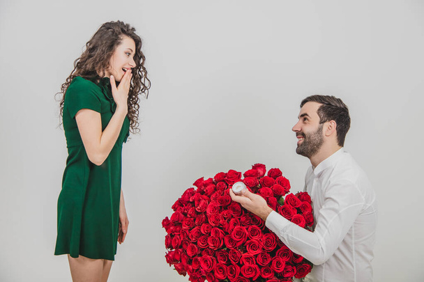 Man asking partner to marry him by giving her a engagement ring and bunch of red flowers, woman is taken aback. - 写真・画像