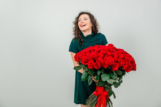 Cheerful young lady with long wavy hair being excited to get bouquet of red roses on Womens day isolated over white background. - Foto, Imagem