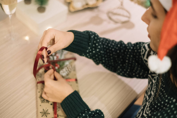 Woman tying Christmas present with red ribbon - Фото, изображение
