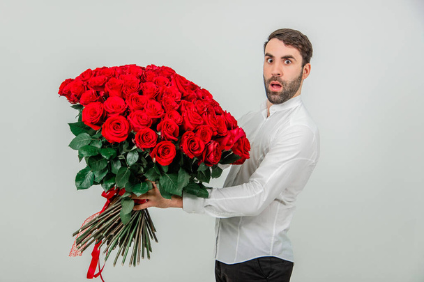 Portrait of a young man with a red roses bouquet, looking confused, because he dont know how to make a proposal. - Photo, image