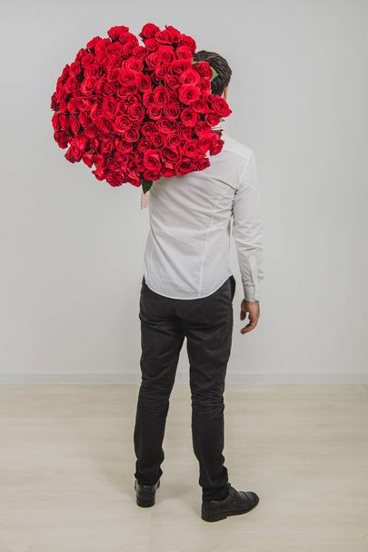 Полный портрет уверенного человека в формальной одежде, стоящего спиной к камере, несущего букет красных роз на плече
. - Фото, изображение