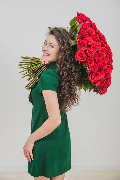 Excited woman isolated over a white background, keeping huge bouquet of tender flowers on her shoulder and looking at the camera fully delighted. - Foto, Bild
