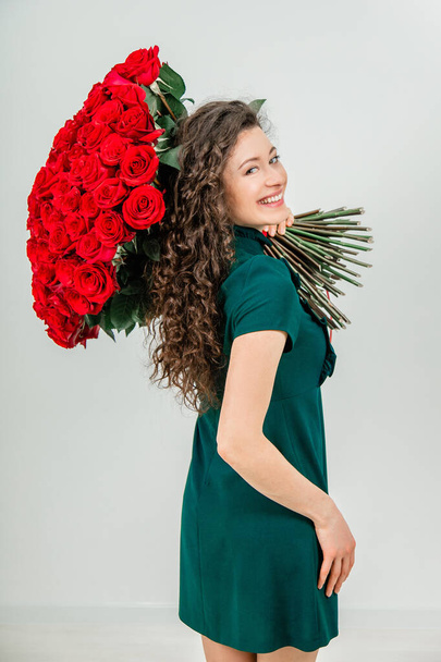 Enthusiastic woman isolated over a white background, keeping huge bouquet of tender flowers on her shoulder and looking at the camera fully delighted. - Фото, зображення