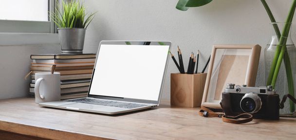 Cropped shot of comfortable workspace with blank screen laptop computer, office supplies and camera on wooden table  - 写真・画像