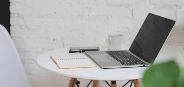 Обрезанный снимок удобного рабочего места на открытом пустом экране ноутбука и офисных принадлежностей на белом столе
  - Фото, изображение