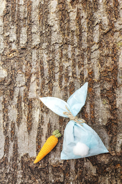 Velikonoční zajíček (králičí) papírový dárkový obal s nápadem na pletenou mrkev. Koncept řemeslné výroby pro děti (děti). Na dřevěném pozadí kůry - Fotografie, Obrázek