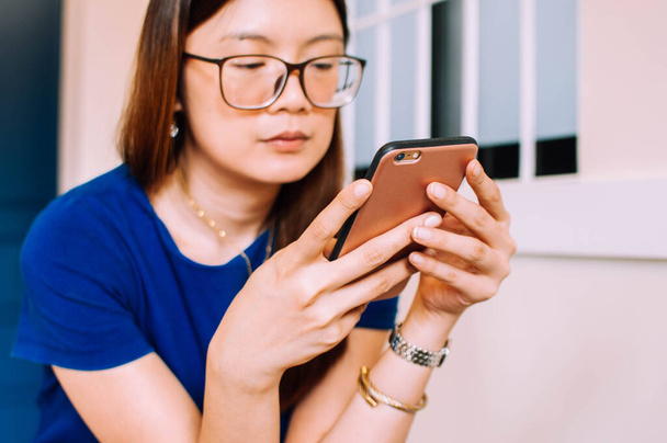 eine junge asiatische Frau in Freizeitkleidung benutzt drinnen ein Smartphone - Foto, Bild