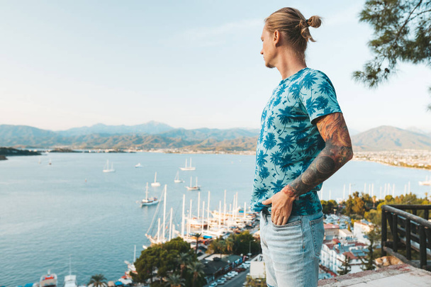 Handsome blond man standing at viewpoint with view on port in Fethiye - Foto, afbeelding