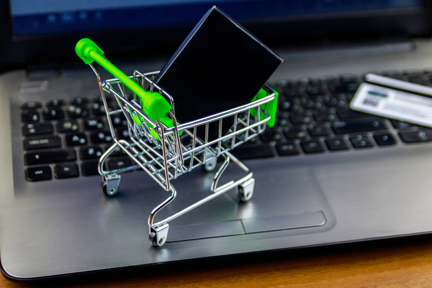 Online vásárlási koncepció. Kis bevásárlókosár a dobozban és hitelkártyával a laptop billentyűzet - Fotó, kép
