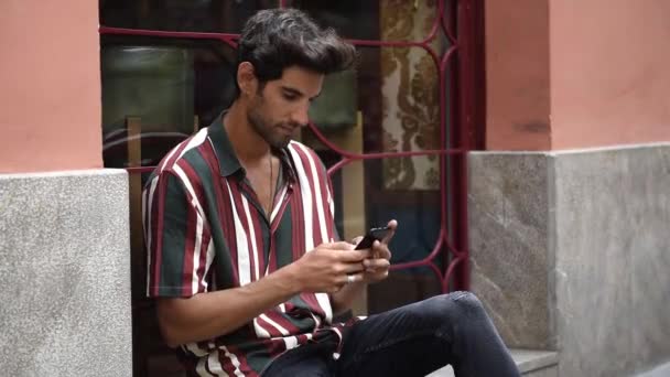 Nuori mies käyttää älypuhelinta istuu kaupunkien askel
. - Materiaali, video