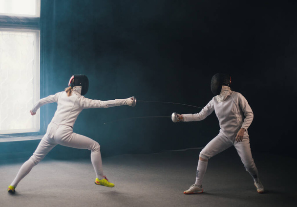 A fencing training in the studio - two women in protective costumes having a duel - pointing swords at each other - Photo, Image