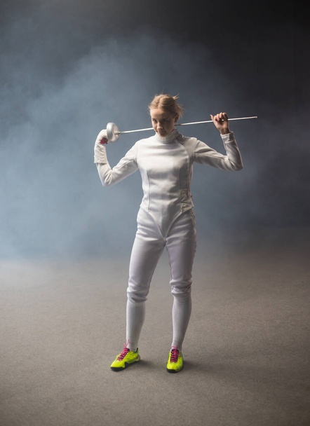 A young woman fencer standing in the studio with a sword behind her shoulders - Foto, Bild