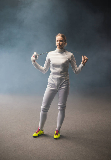 A young woman fencer in yellow shoes standing with a sword behind her shoulders - Photo, Image