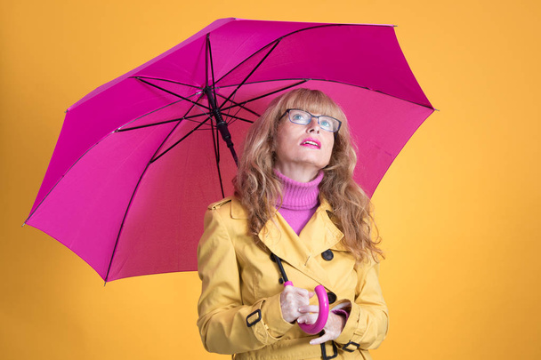ενήλικη γυναίκα με ανοιχτή ομπρέλα κοιτάζοντας σε κίτρινο φόντο - Φωτογραφία, εικόνα