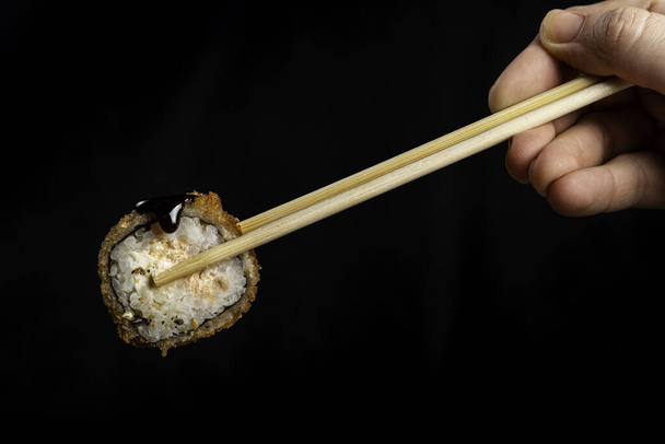 Breaded Sushi - Hot Roll. Woman picking sushi with chopstick. Black background. - Photo, Image
