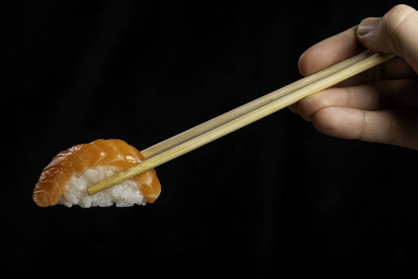 Nigiri Sushi. Woman picking sushi with chopstick. Black background. - Фото, изображение