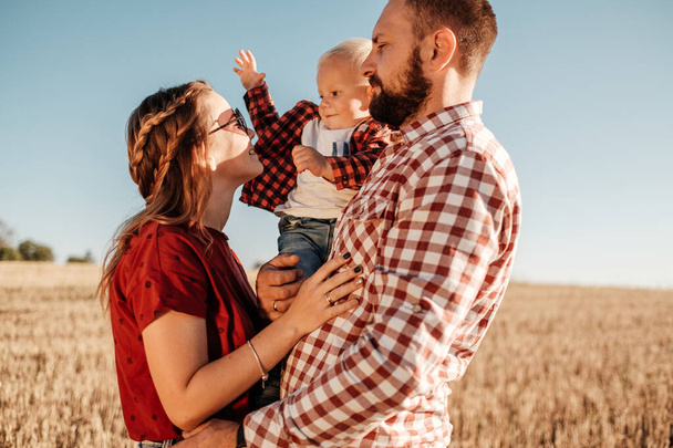 Happy Young Family Mom and Dad with Their Little Son Enjoying Summer Weekend Picnic Outside the City in the Field at Sunny Day Sunset, Vacation Time Concept - Photo, Image