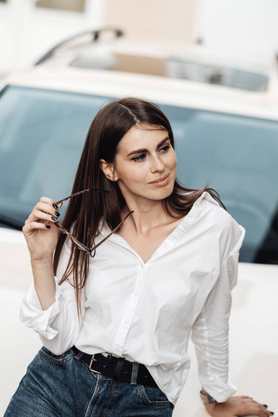 Close Up Portret jednej stylowej młodej kobiety ubranej w dżinsy i białą koszulę pozowanie w pobliżu samochodu, Business Lady, Kobieta Power Concept - Zdjęcie, obraz