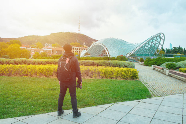 viajero con la cámara en la mano de pie frente al Puente de la Paz, uno de los sitios más importantes de Tiflis Georgia
. - Foto, Imagen