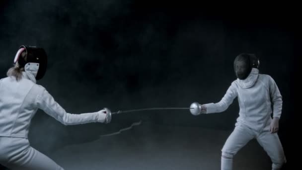 Trening szermierki - dwie kobiety pojedynkujące się w ciemnym studio - Materiał filmowy, wideo