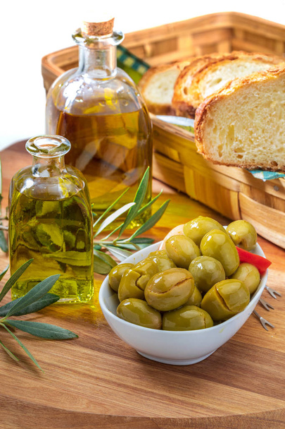 Artisan olives (canned in extra virgin olive oil, vinegar, spices) with red peppers and garlic. Includes olive tree leaves, slices of bread and bottle of extra virgin olive oil. Appetizer concept. On  - Foto, afbeelding