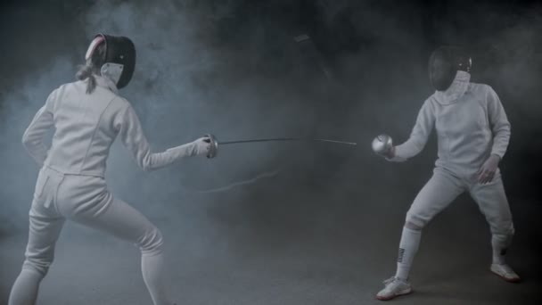 Schermtraining - twee jonge vrouwen die een duel hebben in de rokerige studio - Video