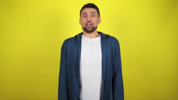 Ein junger Mann in blauem Hemd und weißem T-Shirt ist überrascht und blickt in die Kamera. gelber Hintergrund mit Kopierraum. 4k Zeitlupe - Filmmaterial, Video