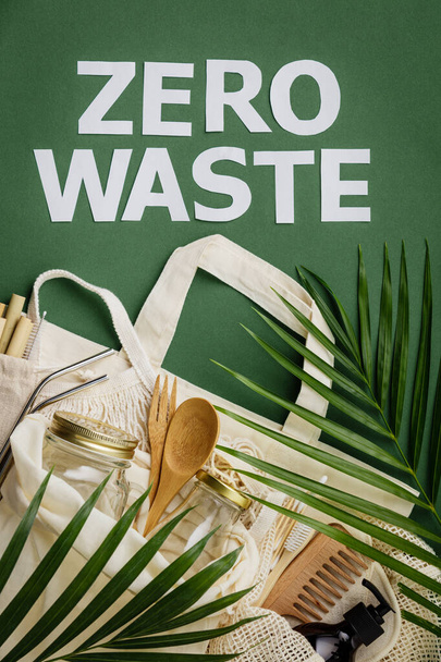 廃棄物ゼロのコンセプト。緑の背景にコットンバッグ、竹料理、ガラス瓶、竹歯ブラシ、ヘアブラシとストロー - 写真・画像