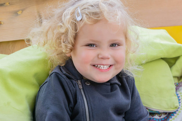 Wesoły uśmiech blondynka mała dziewczynka siedzi na pomarańczowym krześle w kawiarni na zewnątrz - Zdjęcie, obraz
