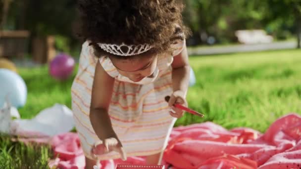 Niña africana está jugando con pinceles y marcadores en el parque con globos multicolores sobre fondos
 - Metraje, vídeo