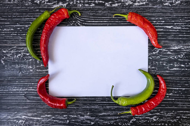 Chili peper en wit papier op een zwarte houten achtergrond. - Foto, afbeelding