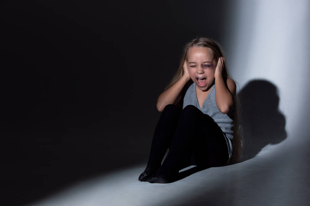 Sad and frightened little girl with bloodshot and bruised eyes sitting scared - Photo, Image