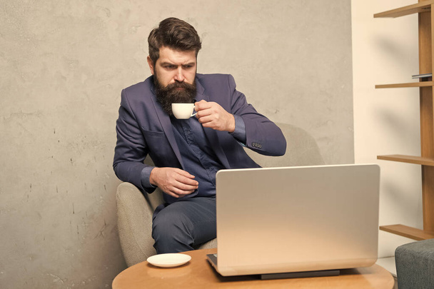 I drink tons of coffee. Serious businessman working at laptop with cup of hot drink. Bearded computer man enjoying his drink break in office. Hard working with tasty drink - Zdjęcie, obraz