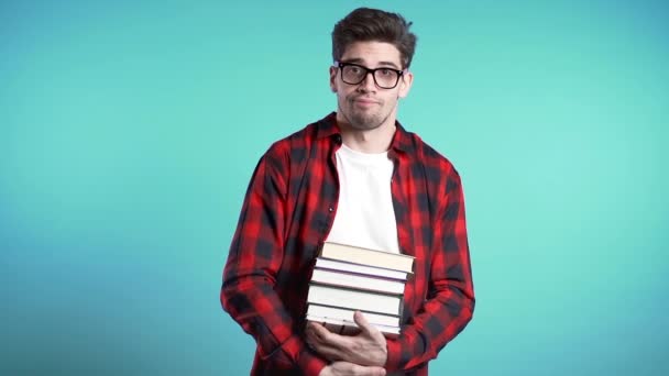 European student on blue background is dissatisfied with amount of homework and books. Man confused, he is annoyed, discouraged frustrated by studies. - Video, Çekim