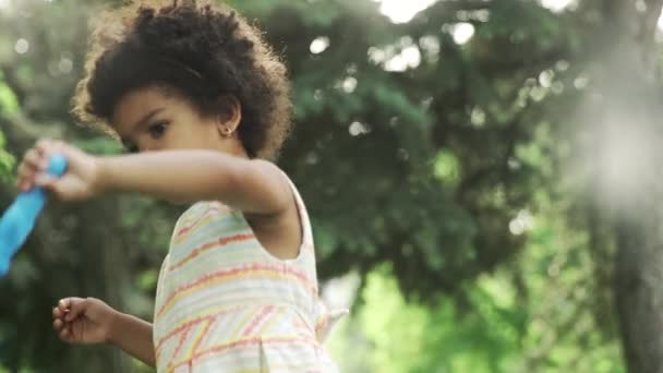 Маленька афроамериканська дівчинка грає з мильними бульбашками в парку
. - Кадри, відео